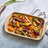 Roasted vegetables on medium rectangular stoneware bar pan with a striped cloth in the background.