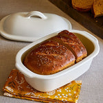 Loaf of bread in a white ceramic dish with a yellow floral napkin underneath.