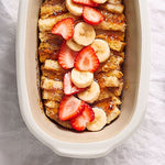 Baked French toast casserole with strawberries and bananas in white, mini-deep stoneware covered baking dish.