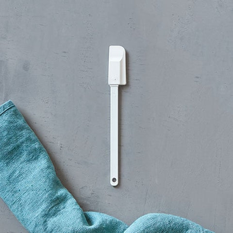 White, mini, skinny kitchen scraper spatula on a gray surface with a teal towel partially visible.