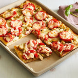 Pizza-style flatbread with tomato and cheese on a natural clay, rectangular baking tray.