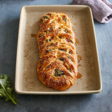 Braided bread loaf on a natural clay, rectangular baking tray with a blue background.