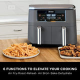 Ninja air fryer with plates of fries and fried chicken on a kitchen counter.