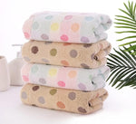Stack of polka dot towels on a white surface with green leaves in the background