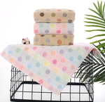 Stack of polka dot towels on a black wire basket with a green leafy plant in the background.