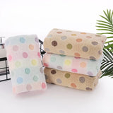 Set of polka dot towels in pastel colors on a white surface with a plant in the background.
