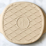 Round beige personal pizza stoneware with wavy patterns on a white background.
