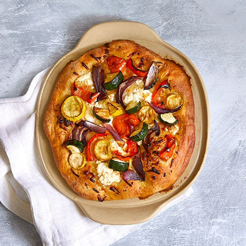 Veggie pizza with various toppings on a personal-sized, round, pizza stoneware.