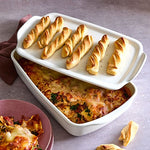 White dish with baked pasta and breadsticks on a gray surface