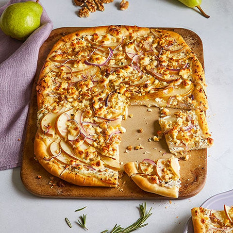 Pizza with pears and onions on rectangular stoneware baking sheet with a slice missing, on a light background.