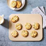 Cookies on rectangular stoneware baking sheet with a cup of coffee and plate in the background.