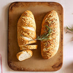 Two loaves of bread on rectangular stoneware baking sheet with a sprig of rosemary.