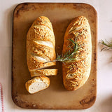 Two loaves of bread on rectangular stoneware baking sheet with a sprig of rosemary.