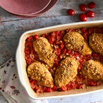 Breaded chicken in a rectangular stoneware baking and serving dish on a rustic wooden surface with napkin to the side.