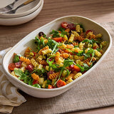 Pasta salad with vegetables in a white, ceramic serving dish on a wooden table.