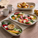 Table setting with a salad in ceramic platter, bread in ceramic serving dish, and ceramic mugs on a wooden surface.