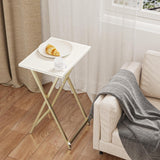 Small white folding table with a plate of food next to a beige sofa with a gray blanket.