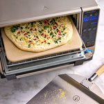 Pizza being baked on small square pizza stoneware in a toaster oven.