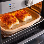 Two pieces of breaded fish cooking in an oven on a stoneware bar pan.
