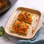 Two pieces of breaded fish on a beige stoneware bar pan with a light background.