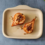 Two roasted pears with nuts on a beige rectangular stoneware bar pan against a blue background.
