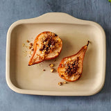 Two roasted pears with nuts on a beige rectangular stoneware bar pan against a blue background.