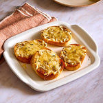 Garlic bread on a white, square stoneware serving tray with a pink cloth to the side.