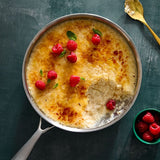Creme bréleé with raspberries in a metal dish on a dark surface.