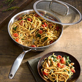 Stir-fried pasta with vegetables in stainless steel cookware pan on a wooden table.