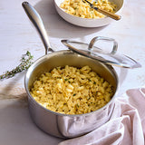 Stainless steel pot with macaroni and cheese on a light wooden surface.