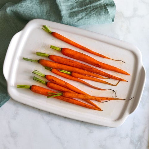 Carrots on Stoneware Serving and Cooking Tray on a white marble surface with a green cloth.