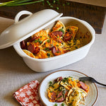 White satin glazed stoneware covered baking dish with cheesy dish and a serving on a plate with a fork.