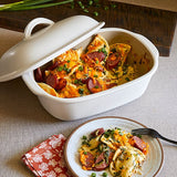 White satin glazed stoneware covered baking dish with cheesy dish and a serving on a plate with a fork.