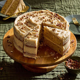 Layered cake with pecans on a wooden cake stand with a slice taken out, on a green textured tablecloth.