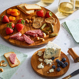 Wooden cake stand converted to two serving platters with assorted snacks including strawberries, salami, and blue cheese on a marble surface.