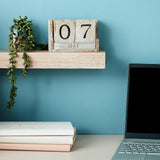 Desk setup with a laptop, books, and a wooden calendar on a wall shelf.