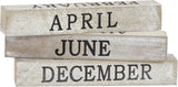 Stack of wooden calendar blocks with months engraved on them against a white background.