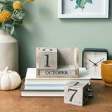 Wooden calendar blocks on books with a clock and decorative items on a table.