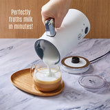 White milk frother being used to froth milk in a glass on a marble surface.