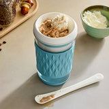 Light blue, frozen drink maker tumbler cup on a table with a spoon and small bowl.