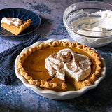 Pumpkin pie in a stoneware pie baking dish with a slice removed, topped with whipped cream.