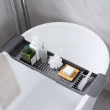 A gray bathtub storage tray attached to a bathtub, holding various bathroom items like a bottle, a brush, and a block.